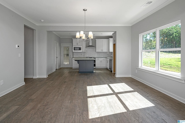 kitchen featuring appliances with stainless steel finishes, wall chimney exhaust hood, decorative light fixtures, a center island, and dark hardwood / wood-style flooring