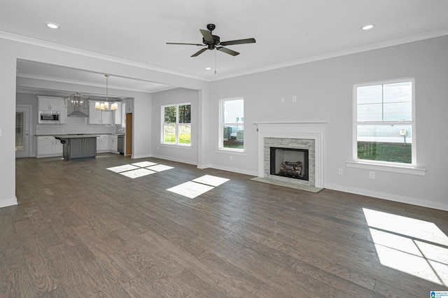 unfurnished living room with ornamental molding, a stone fireplace, dark hardwood / wood-style floors, and ceiling fan with notable chandelier