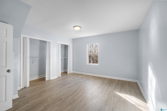 unfurnished bedroom with light hardwood / wood-style floors and multiple closets