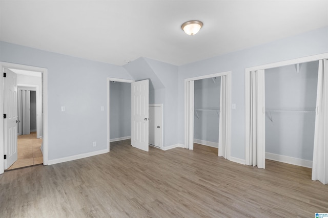 unfurnished bedroom featuring multiple closets and light hardwood / wood-style floors