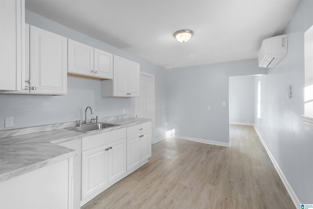 kitchen with a wall unit AC, sink, white cabinets, and light hardwood / wood-style floors