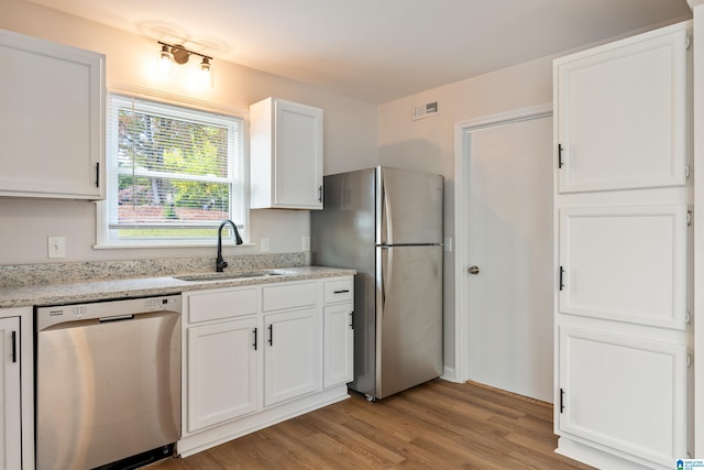 kitchen with light hardwood / wood-style floors, light stone counters, sink, white cabinetry, and appliances with stainless steel finishes