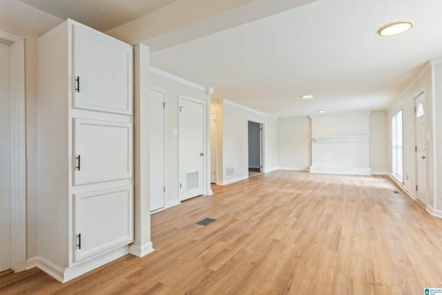 unfurnished living room with ornamental molding, light wood-type flooring, and a brick fireplace