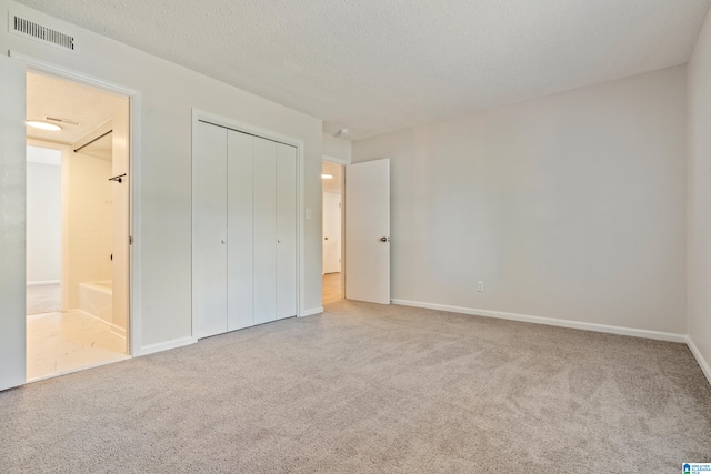 unfurnished bedroom with ensuite bath, a textured ceiling, and a closet