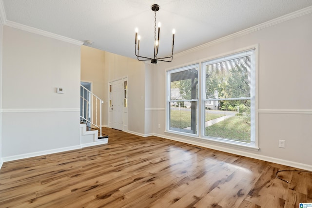 unfurnished dining area with wood-type flooring, a textured ceiling, a chandelier, and ornamental molding