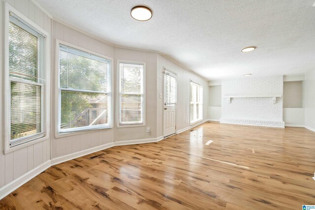 unfurnished living room with light wood-type flooring, a fireplace, and a textured ceiling