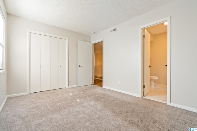 unfurnished bedroom with ensuite bathroom, a textured ceiling, carpet flooring, and a closet