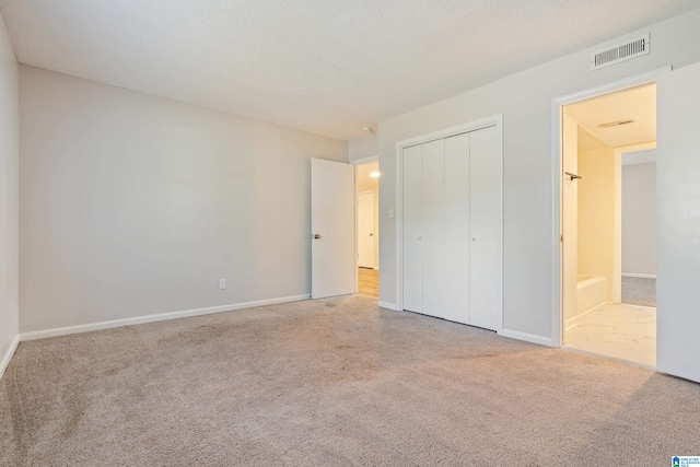 unfurnished bedroom with light carpet, a textured ceiling, and a closet