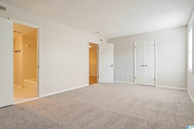 unfurnished bedroom featuring ensuite bathroom, multiple windows, carpet floors, and a textured ceiling