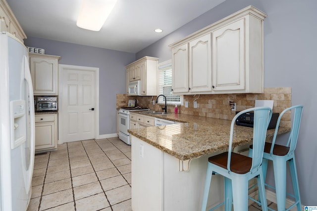 kitchen featuring sink, kitchen peninsula, light stone countertops, backsplash, and white appliances