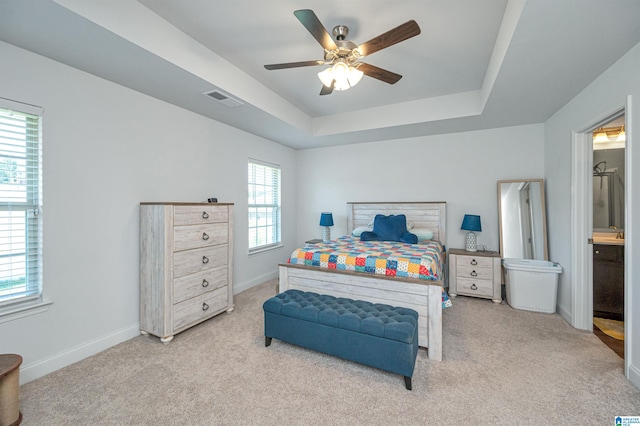 carpeted bedroom featuring ceiling fan, multiple windows, connected bathroom, and a tray ceiling