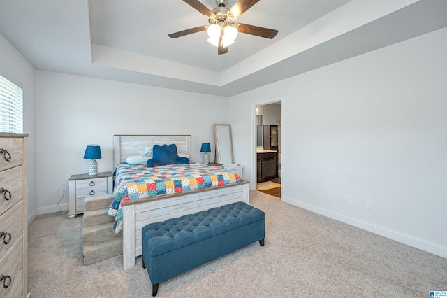 bedroom featuring connected bathroom, a tray ceiling, light carpet, and ceiling fan