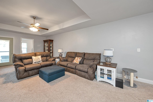 living room with a tray ceiling, ceiling fan, and carpet floors