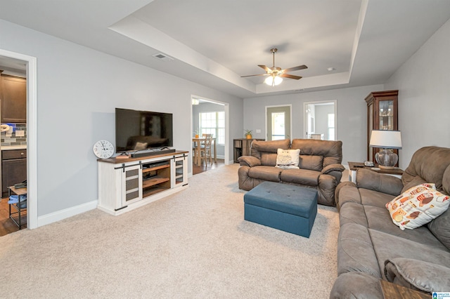 living room with light carpet, ceiling fan, and a raised ceiling