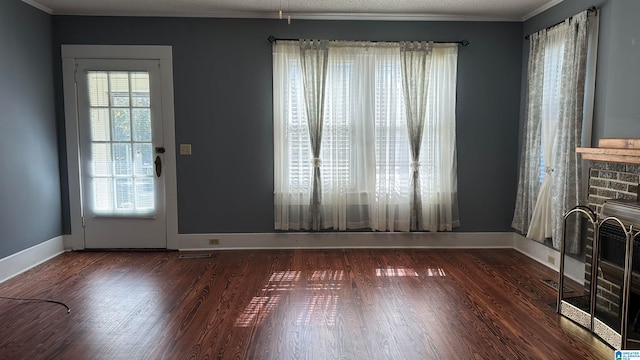 interior space with a brick fireplace, a textured ceiling, dark hardwood / wood-style floors, and crown molding