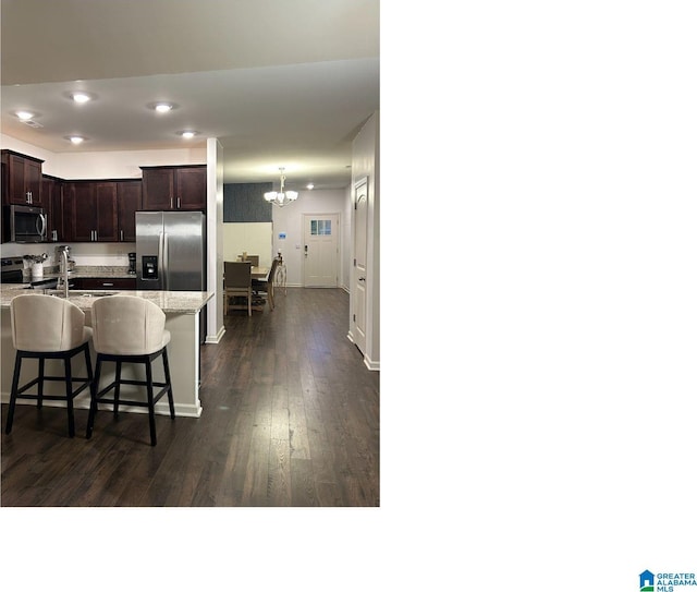 kitchen with stainless steel appliances, light stone countertops, a kitchen bar, a notable chandelier, and dark hardwood / wood-style flooring