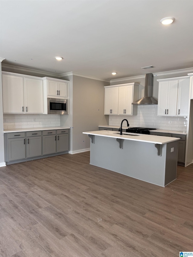 kitchen featuring gray cabinetry, stainless steel microwave, wood-type flooring, and wall chimney range hood