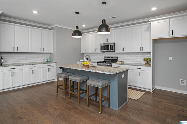 kitchen with stainless steel appliances, white cabinetry, hanging light fixtures, and a center island with sink