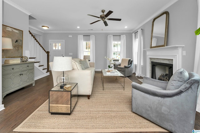 living room featuring hardwood / wood-style floors, ceiling fan, a premium fireplace, and crown molding