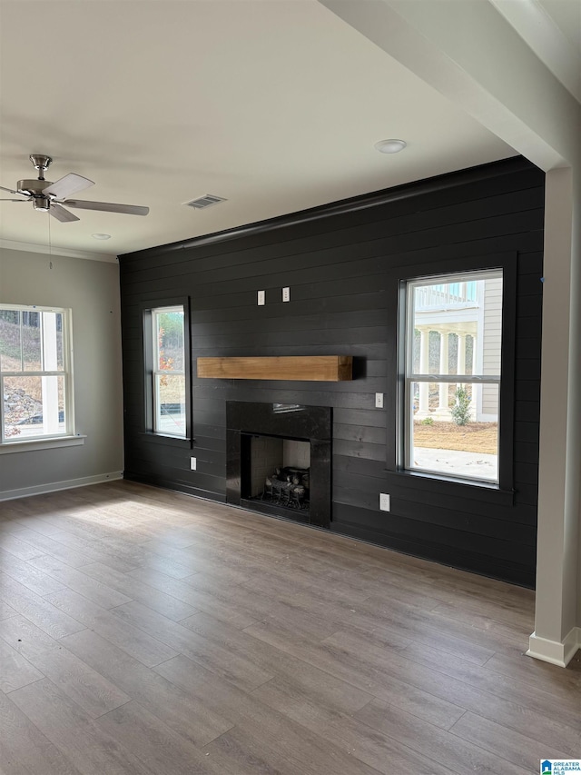 unfurnished living room featuring ceiling fan, wooden walls, and light hardwood / wood-style flooring