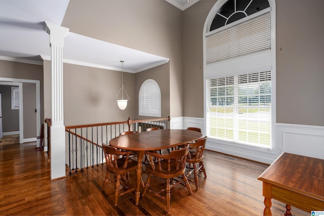 dining space featuring dark wood-type flooring, crown molding, and decorative columns