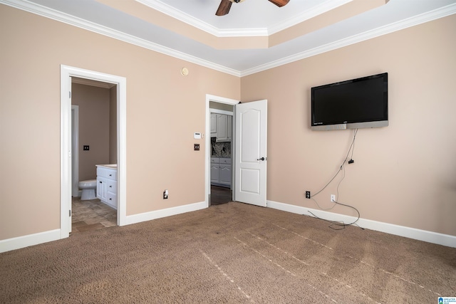 unfurnished bedroom featuring carpet flooring, ornamental molding, ensuite bathroom, ceiling fan, and a tray ceiling