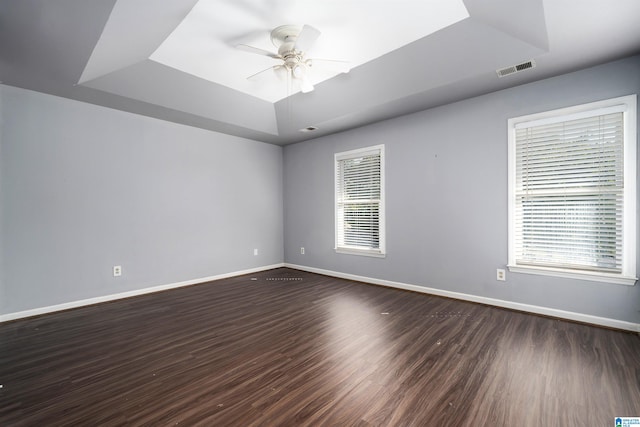 empty room with dark hardwood / wood-style flooring, ceiling fan, and a raised ceiling