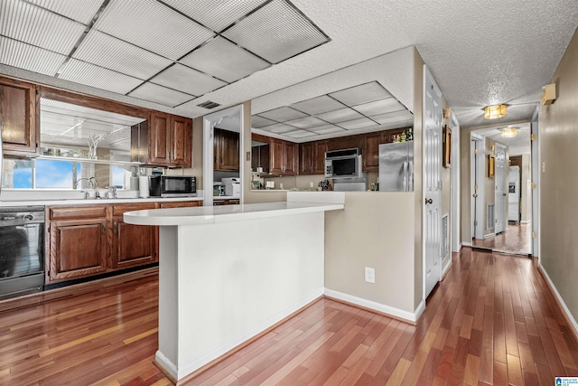 kitchen with wood-type flooring, black dishwasher, kitchen peninsula, sink, and stainless steel fridge