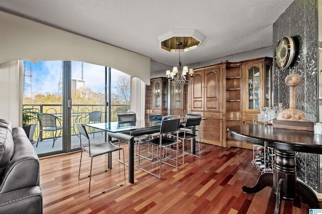 dining room with wood-type flooring, a textured ceiling, and an inviting chandelier