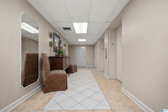 hall with a paneled ceiling and light tile patterned flooring