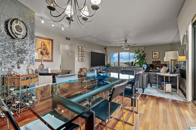 dining area featuring rail lighting, ceiling fan with notable chandelier, and wood-type flooring