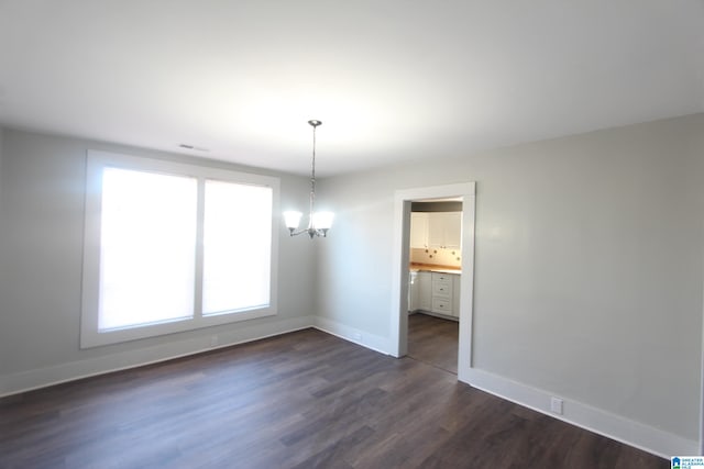 spare room featuring dark wood-type flooring and a chandelier