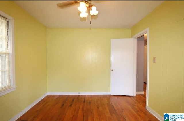 empty room featuring ceiling fan, wood-type flooring, a healthy amount of sunlight, and wooden walls