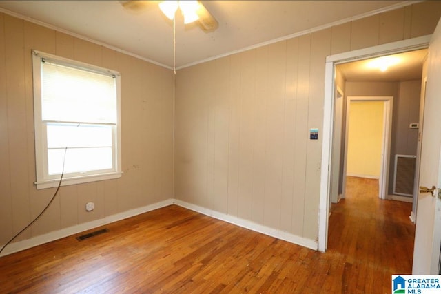 spare room featuring wood walls, a wealth of natural light, hardwood / wood-style flooring, and crown molding