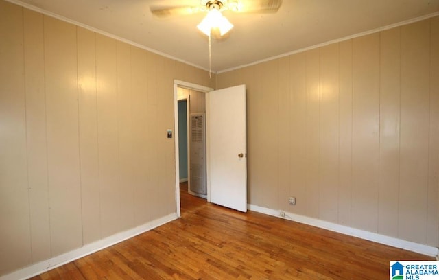 spare room with ornamental molding, wood walls, hardwood / wood-style flooring, and ceiling fan