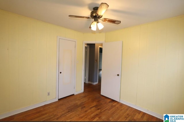 unfurnished bedroom with wood walls, dark wood-type flooring, and ceiling fan