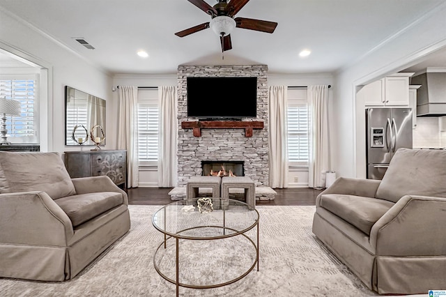 living room with a stone fireplace, hardwood / wood-style floors, ceiling fan, and crown molding