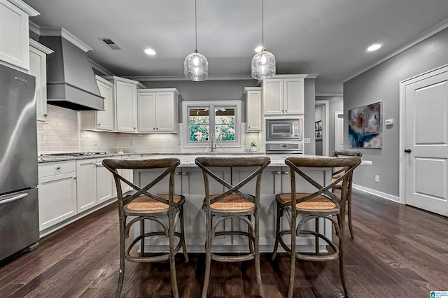 kitchen with dark wood-type flooring, hanging light fixtures, custom exhaust hood, white cabinetry, and appliances with stainless steel finishes