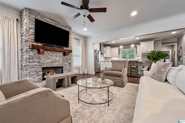 living room featuring light hardwood / wood-style floors, ceiling fan, a stone fireplace, and ornamental molding