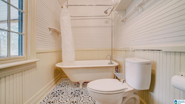 bathroom with tile patterned flooring, a washtub, wood walls, and toilet