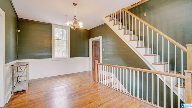 stairway with wood-type flooring, an inviting chandelier, and ornamental molding