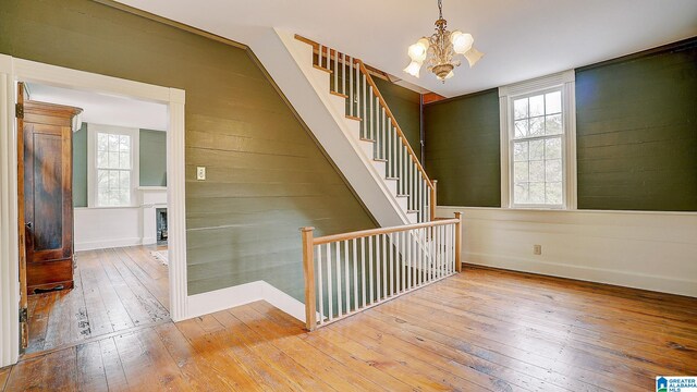 stairs featuring wooden walls, wood-type flooring, and a notable chandelier