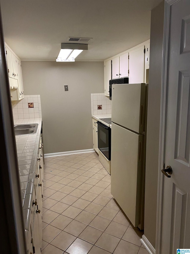 kitchen featuring white cabinets, range, light tile patterned floors, backsplash, and white fridge