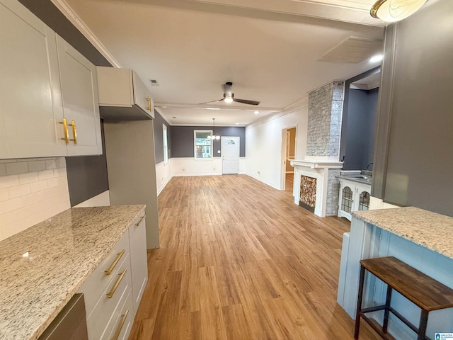 kitchen with light stone countertops, white cabinetry, ceiling fan, and crown molding