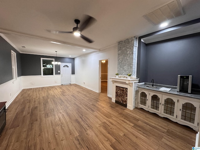 unfurnished living room with wood-type flooring, ceiling fan with notable chandelier, crown molding, and sink