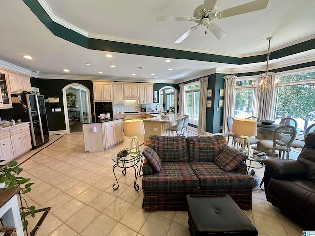 living room featuring a tray ceiling, ceiling fan with notable chandelier, light tile patterned floors, and ornamental molding