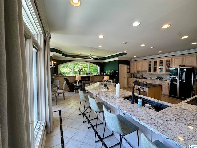 kitchen with tasteful backsplash, light stone counters, crown molding, a kitchen bar, and black refrigerator