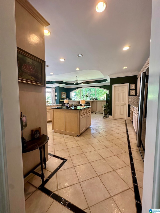 kitchen with crown molding, a kitchen island, backsplash, light tile patterned floors, and light brown cabinets