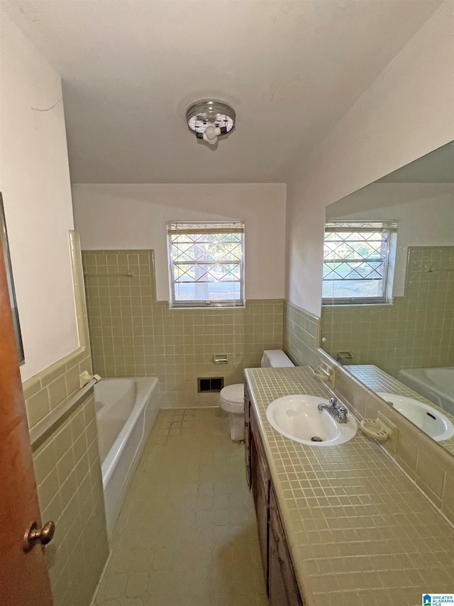 bathroom with tile walls, healthy amount of natural light, a tub to relax in, wainscoting, and toilet