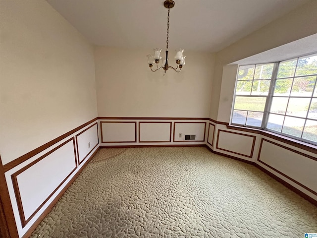 unfurnished room with a decorative wall, a chandelier, a wainscoted wall, and light carpet